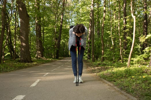 Woman bends over leaning walking poles feeling pain, not well while doing sport, jogging, Nordic walk in Park.Hard breathing, Dizziness. Sickness during incorrect workout. Horizontal Plane, Copyspace