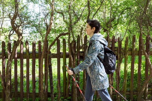 Nordic walking. Caucasian Woman Walks With Trekking Poles And Backpack, Physical Activity In Countryside . Sport Tourism, Outdoor Activity, Recreation. Horizontal Plane High quality photo