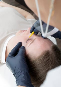 Beautician, Beauty Master Combing Eyelashes Of Caucasian Beautiful Client After Lamination Procedure, Treatment In Beauty Salon. Closeup, Vertical Plane. High quality photo