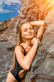 Woman travel sea. Attractive blonde woman in a black swimsuit enjoying the sea air on the seashore around the rocks. Travel and vacation concept