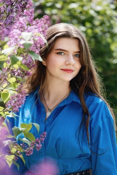 Portrait of a beautiful young woman surrounded by lilac flowers. Spring blossom.