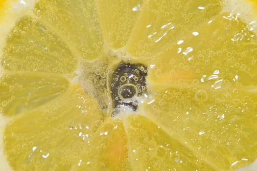 Slice of ripe lemon in water. Close-up of lemon in liquid with bubbles. Slice of ripe citron in sparkling water. Macro image of fruit in carbonated water