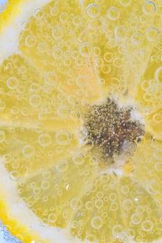 Close-up of a lemon slice in liquid with bubbles. Slice of ripe lemon in water. Close-up of fresh citron slice covered by bubbles. Macro vertical image