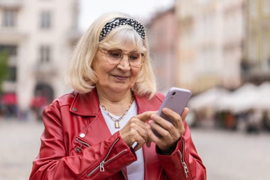 Portrait of senior woman using smartphone typing text messages looking for a way on map in mobile navigator app outdoors. Elderly grandmother walking in urban city street background. Town lifestyles
