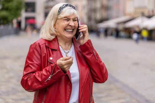 Happy senior woman having remote conversation communicate speaking by smartphone. Old grandmother talking on phone unexpected good news gossip walking in urban city street. Town lifestyles outdoor