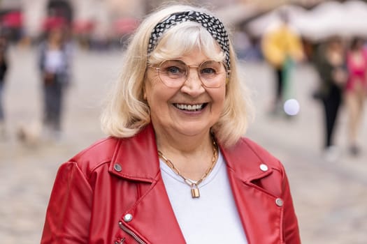 Portrait of happy senior woman smiling friendly, glad expression looking at camera dreaming, resting, relaxation feel satisfied good news outdoors. Elderly grandmother in urban flowered city street