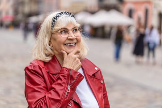 Thoughtful pensive puzzled senior woman with pensive expression, pondering a solution, doubting question, thinking inspiration dreaming outdoors. Elderly grandmother in city street. Town lifestyles