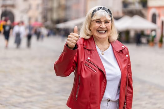 Like. Happy senior woman looking approvingly at camera showing thumbs up, like sign positive something good positive feedback. Elderly grandmother walking in urban city street. Town lifestyles outdoor