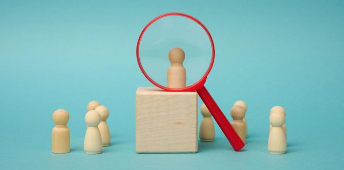 wooden figures of men stand on a beige background and a red plastic magnifying glass. Recruitment concept, search for talented and capable employees, career growth