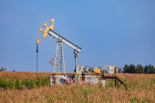 The old oil pump in a field under blue sky