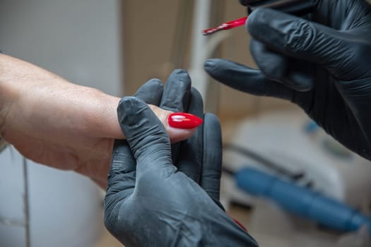 A master manicurist covers the renewed nails of the client with red varnish, Manicure process in beauty salon, High quality photo