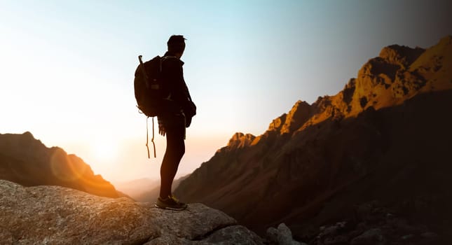 A young man travels, climbs trails among the high red mountains, the traveler is hiking and admiring the sunset in a picturesque place.