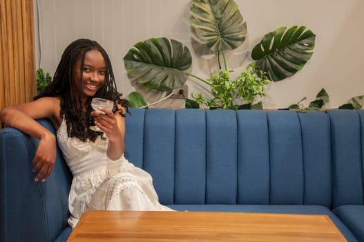 copyspace of relaxed young african american woman with a glass of liquor looking at camera and leaning on a blue sofa. High quality photo