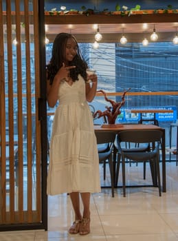 young afro woman standing leaning against a door looking up with a colored cocktail in her hand. High quality photo