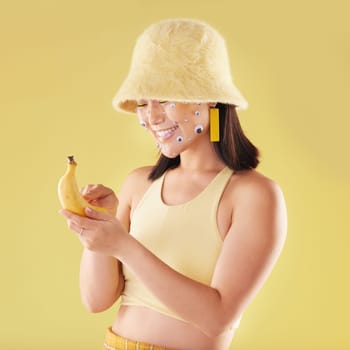 Woman, banana phone texting and studio with smile, communication and eyes sticker art on face. Asian model girl, yellow background and fashion with beauty, aesthetic and cosmetic wellness with fruit.