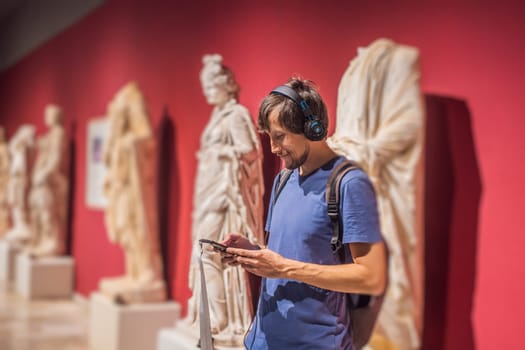Portrait of contemporary man looking at sculptures and listening to audio guide at museum exhibition.