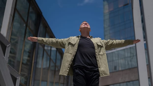 A happy man stands against the backdrop of a skyscraper with his arms spread out to the sides like wings