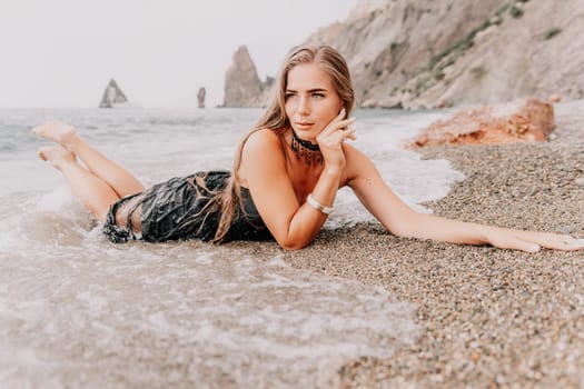 Woman travel sea. Young Happy woman in a long red dress posing on a beach near the sea on background of volcanic rocks, like in Iceland, sharing travel adventure journey