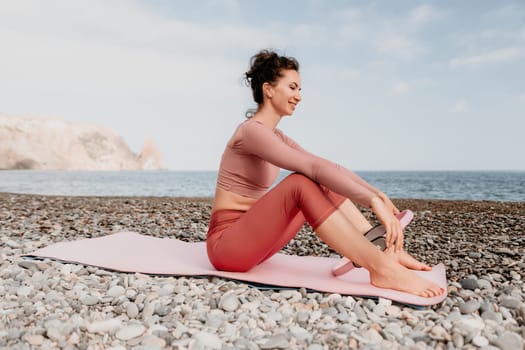 Middle aged well looking woman with black hair doing Pilates with the ring on the yoga mat near the sea on the pebble beach. Female fitness yoga concept. Healthy lifestyle, harmony and meditation.