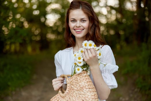close portrait of a happy, red-haired woman with a wicker basket full of daisies in nature. High quality photo