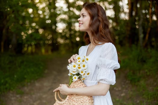 close portrait of a happy, red-haired woman with a wicker basket full of daisies in nature. High quality photo