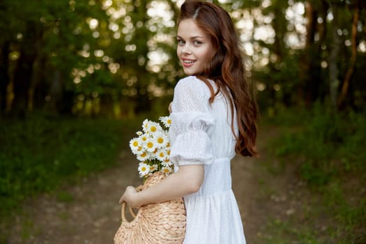 close portrait of a happy, red-haired woman with a wicker basket full of daisies in nature. High quality photo