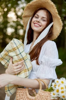 a woman with a wicker hat, a bag and a plaid smiles while standing in nature in the park. High quality photo