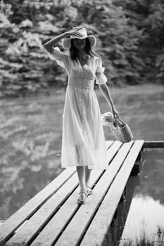 monochrome photo of a woman on the pier of a forest lake with a wicker hat looking at the camera. High quality photo