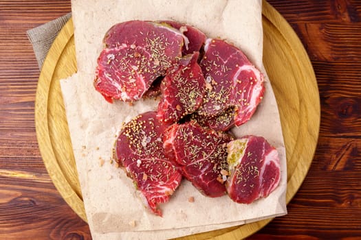 Fresh raw chopped beef on a wooden cutting board with spices, herbs and vegetables, top view. Flat lay