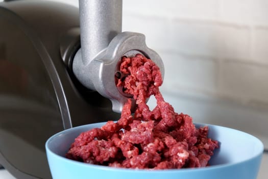 Cooking at home in the kitchen working with beef meat on an electric meat grinder. Close up, selective focus