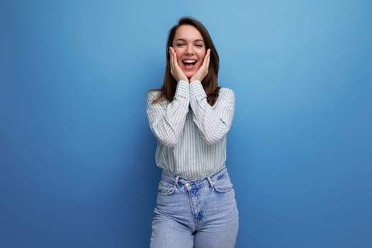 european young brunette female adult in a striped shirt and jeans with hair below her shoulders in a studio background.