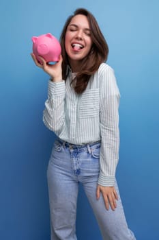 cute 20s brunette lady in shirt and jeans saved up her money for a dream in a piggy bank.