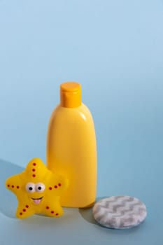 An empty yellow bottle of baby soap or washing gel and cleansing sponge. Accessories above blue background. Template for design