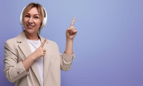 portrait of young woman in wireless headphones pointing finger at copy space studio background.