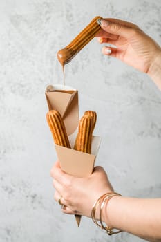 Woman taking churros from a cone and dipping it in chocolate sauce