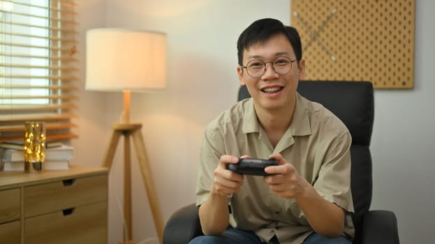 Man in casual clothes and glasses holding wireless controller playing video game. Entertainment, technology and hobby concept.