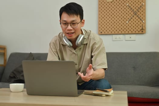 Handsome young adult man looking at laptop, talking on video call with coworkers in online briefing from home.