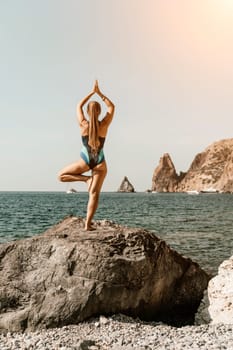 Yoga on the beach. A happy woman meditating in a yoga pose on the beach, surrounded by the ocean and rock mountains, promoting a healthy lifestyle outdoors in nature, and inspiring fitness concept