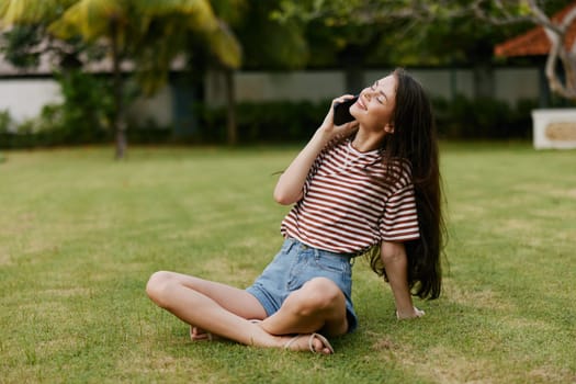 woman using t-shirt blogger tree grass park lifestyle healthy browsing student nature smiling phone app outside happy palm human sitting green person