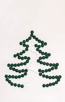 White background, medicine mockup, Christmas tree made of green white pills,tablets,vitamins spirulina. Merry Christmas, Happy New Year concept, pharmacy postcard,flatly, top view, copy space Vertical