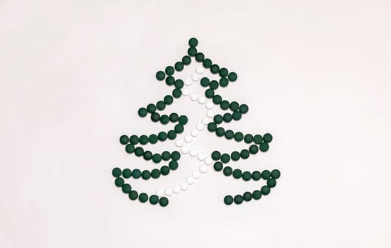 White background, medicine mockup, Christmas tree made of green white pills,tablets,vitamins spirulina. Merry Christmas, Happy New Year concept, harmacy postcard,flatly, top view,copy space Horizontal