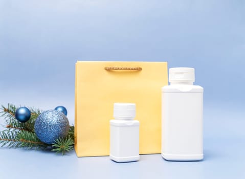Christmas pharmacy two white bottles of pills, golden paper package, Christmas tree, sparkling toy balls on blue background. Winter holidays, medical concept. Horizontal plane