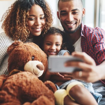 Cropped shot of a happy young family of three taking selfies together in their living room at home.