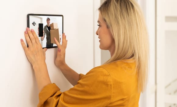 Woman watching delivery man on security camera cctv video on tablet.