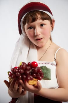 Portrait of Little girl in a stylized Tatar national costume with berries and a brush of grapes on a white background in the studio. Photo shoot of funny young teenager who is not a professional model