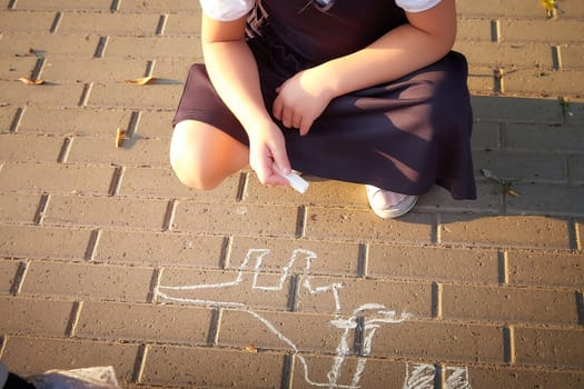 Little girl of elementary school student in modern school uniform drawing with chalk on asphalt outdoors. Female child schoolgirl going to school. Back to school in september 1