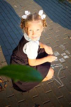 Little girl of elementary school student in modern school uniform drawing with chalk on asphalt outdoors. Female child schoolgirl going to school. Back to school in september 1