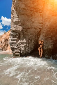 Woman swimsuit sea. Attractive blonde woman in a black swimsuit enjoying the sea air on the seashore around the rocks. Travel and vacation concept