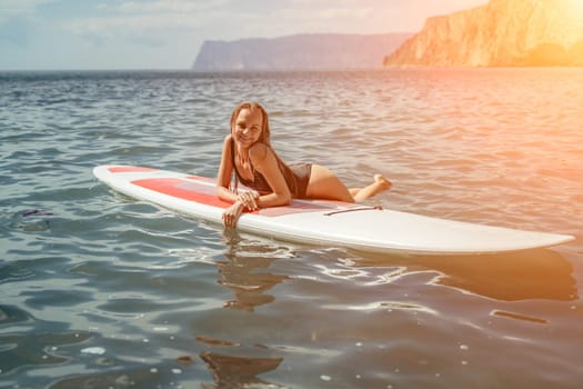 Woman sup sea. Sports girl on a surfboard in the sea on a sunny summer day. In a black bathing suit, he sits on a sapa in the sea. Rest on the sea