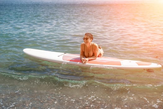 Woman sup sea travel. Sports girl on a surfboard in the sea on a sunny summer day. In a black bathing suit, he sits on a sapa in the sea. Rest on the sea